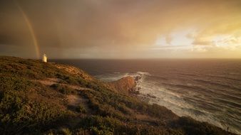 rainbow over a lighthouse on a rocky coast