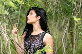 brunette in a black dress on a background of green forest