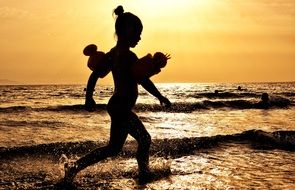 little girl runs along the beach at sunset