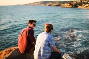 friends are sitting on a stone near the water