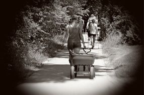 woman with wheelbarrow and people with sticks walking Away by path