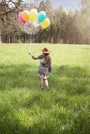 little girl with colorful balloons among green meadow