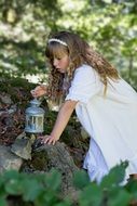Blonde child Girl in white gown with Lantern in garden