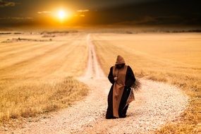 Monks walking on soil road through harvested fields at sunset