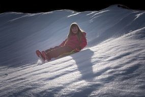 girl in a pink suit is sledding from the mountain