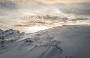 Cross on a snowy hill at colorful sky background