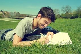 a man writes a letter while lying on green grass