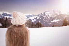 girl with long hair wearing a hat among snowy mountains