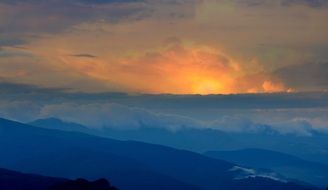 yellow sun through thick clouds above the mountains
