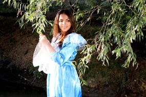 Rirl in a long blue dress under a beautiful, green willow tree