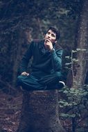 pensive young man sitting on a stump in the forest