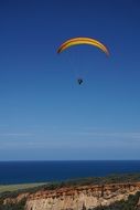paraglider in bright blue sky over colorful landscape