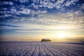 barn on arable field covered with snow at sunrise