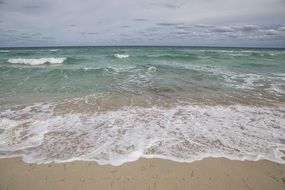 foamed waves splashing on Sand Beach at cloudy day