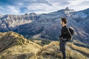 young man with backpack stands on mountain peak looking at beautiful landscape