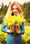 Blonde woman with the bouquet of beautiful, wild, yellow flowers near the green trees