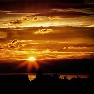 silhouettes of buildings on the coast against a bright sun and a golden sky