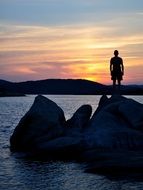 man stands on a boulder by the sea on a sunset background