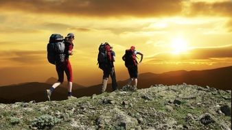 three tourists with backpacks in the mountains at sunset