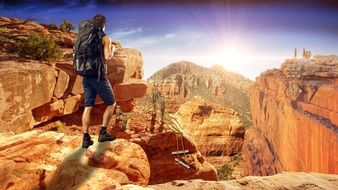 hiker with backpack on top of mountain formation in the bright sun