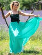 Blonde Girl in green dress swinging above the green and yellow grass