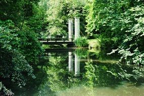 Bridge over the clear pond among the green trees