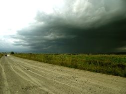 thunderclouds over a dirt road along the field