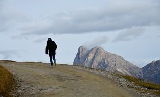 Wanderer, man walking away on soil road in Dolomites