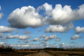 Fluffy Clouds at blue Sky above Forest and Road