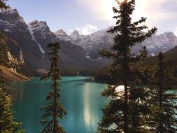Green spruce trees at beautiful turquoise Lake in scenic Mountain valley with snowy mountains
