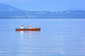 man and woman in Rowing Boat on water in view of green mountain coastline