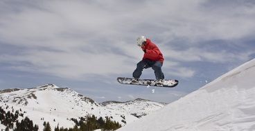 Person jumping while snowboarding on the beautiful snowy mountains