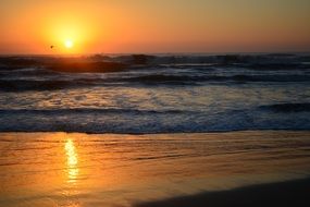 reflection of the orange sun on a sandy beach at sunset