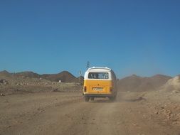 yellow-white bus rides along a dusty mountain road