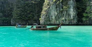 wooden boats on bright turquoise water off the coast of Thailand