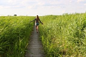 girl on a wooden path among tall green grass