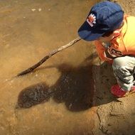 boy in a cap playing with a stick in the lake