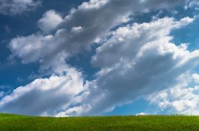 white clouds on blue sky over a green hill