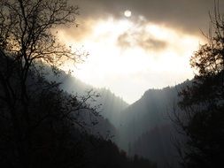 sun behind the clouds over the dark mountains