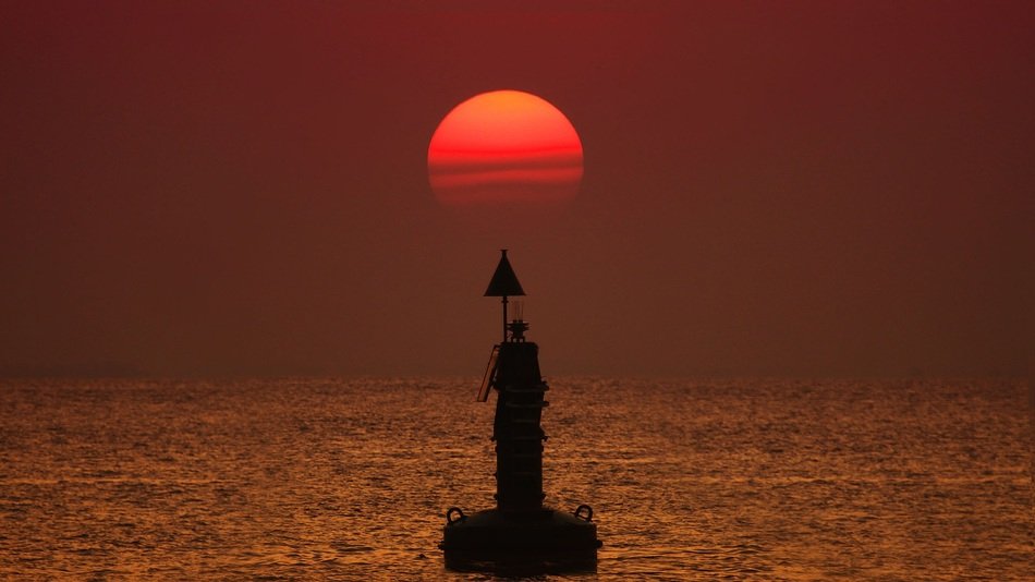 red sun above Buoy on water in dusk