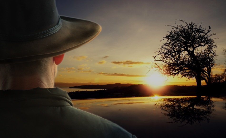 Cowboy in the hat watches a bright and colorful sunrise on beautiful landscape