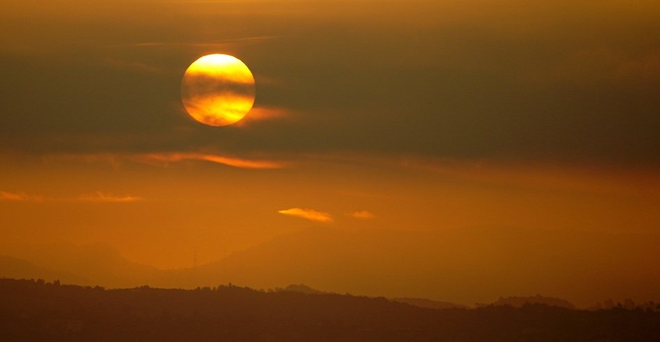Sunset Sun hides in dark Clouds above mountains