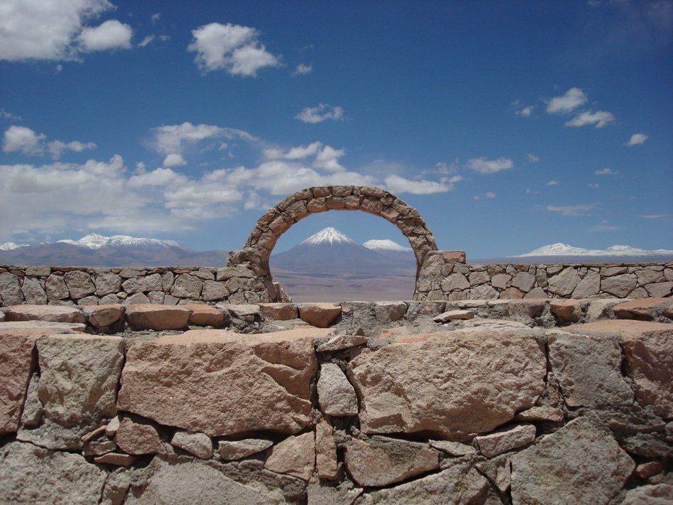 distant view of Volcano in Desert through arch in stone fence