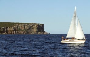 white sailing boat on sea at rocky coast