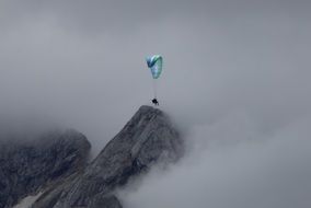 landscape of man on a blue parachute on top of a foggy mountain