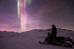 man on Snowmobile looking at aurora borealis in starry sky, arctic