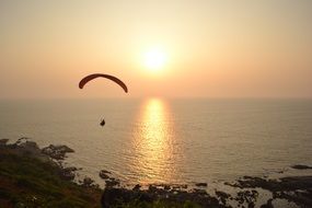 Paragliding with parachute over the beautiful ocean at colorful sunset