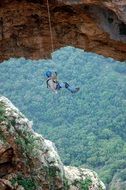 Person hanging on a rope on the mountain above the green tree