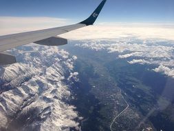 wing of flying airplane over alpine mountains