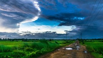 dramatic sky over rural road in green field